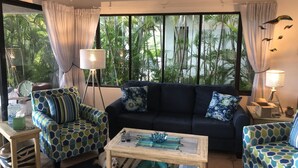 A living room with a dark blue sofa, patterned armchairs, a wooden coffee table, and a view of tropical foliage through large windows. - Casa Da'Vida In Playa Hermosa, Guanacaste, Costa Rica (Playa Hermosa)
