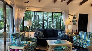 A spacious living room with a large window, a ceiling fan, and a view of palm trees. - Casa Da'Vida In Playa Hermosa, Guanacaste, Costa Rica (Playa Hermosa)