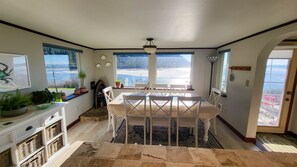 Un espace repas comprenant une table et des chaises, de grandes fenêtres donnant sur la plage et un luminaire au plafond.