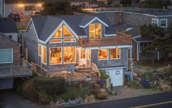 Une maison à deux étages dotée d’un balcon, de grandes fenêtres et d’un intérieur bien éclairé.