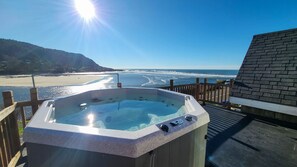 Un bain à remous avec une terrasse en bois, offrant une vue sur la plage et l’océan.