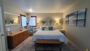 Une chambre d’hôtel comprenant un lit, des tables de chevet, une commode, un banc et des œuvres d’art accrochées aux murs.