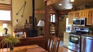A cozy living room with a fireplace, wooden furniture, and a kitchen with modern appliances.
