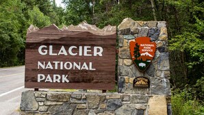 A sign for Glacier National Park with a stone base and a wooden signboard.