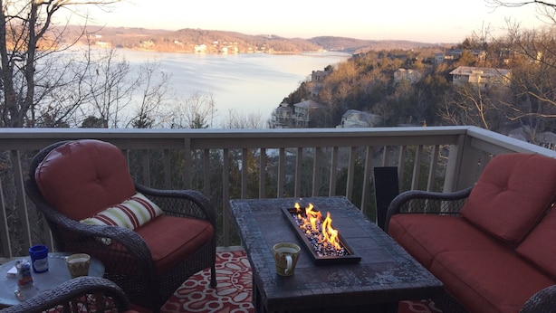 Een terras met rieten meubilair, een vuurplaats en uitzicht op een meer en heuvels.