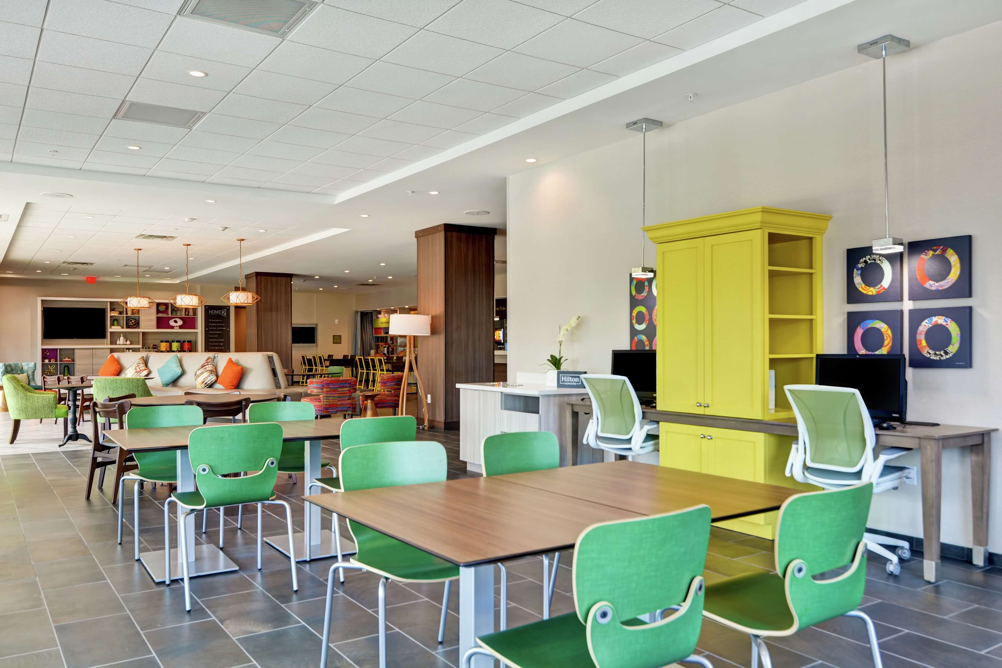 Um hall de hotel moderno com cadeiras verdes, um balcão de recepção de madeira e um armário amarelo.
