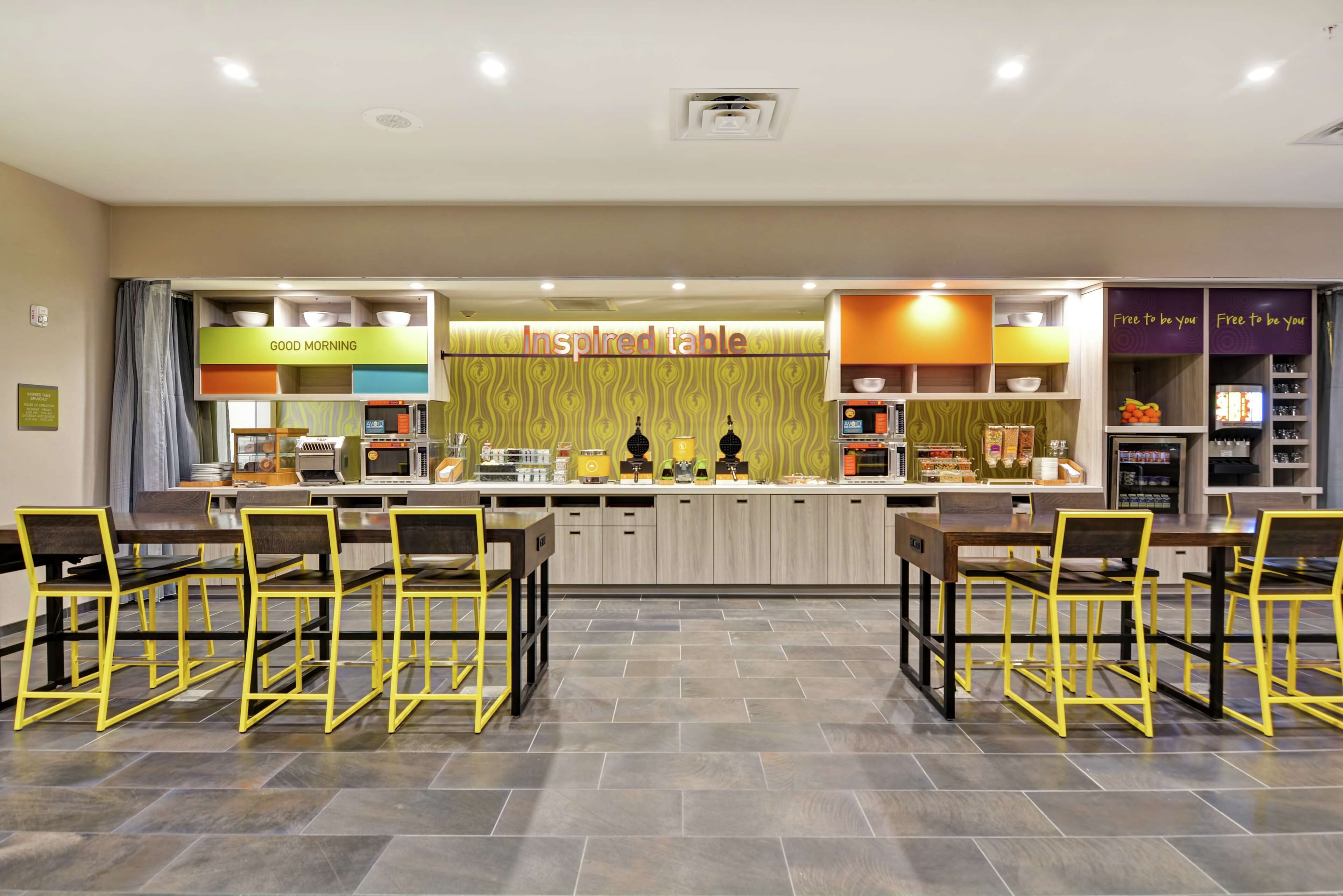 A modern restaurant with a central counter, yellow chairs, and a variety of dishes displayed.
