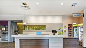 Eine moderne Hotelrezeption mit klarem Design, einer digitalen Check-in-Station, einer Minibar und einer Selbstbedienungsgetränkeautomaten.