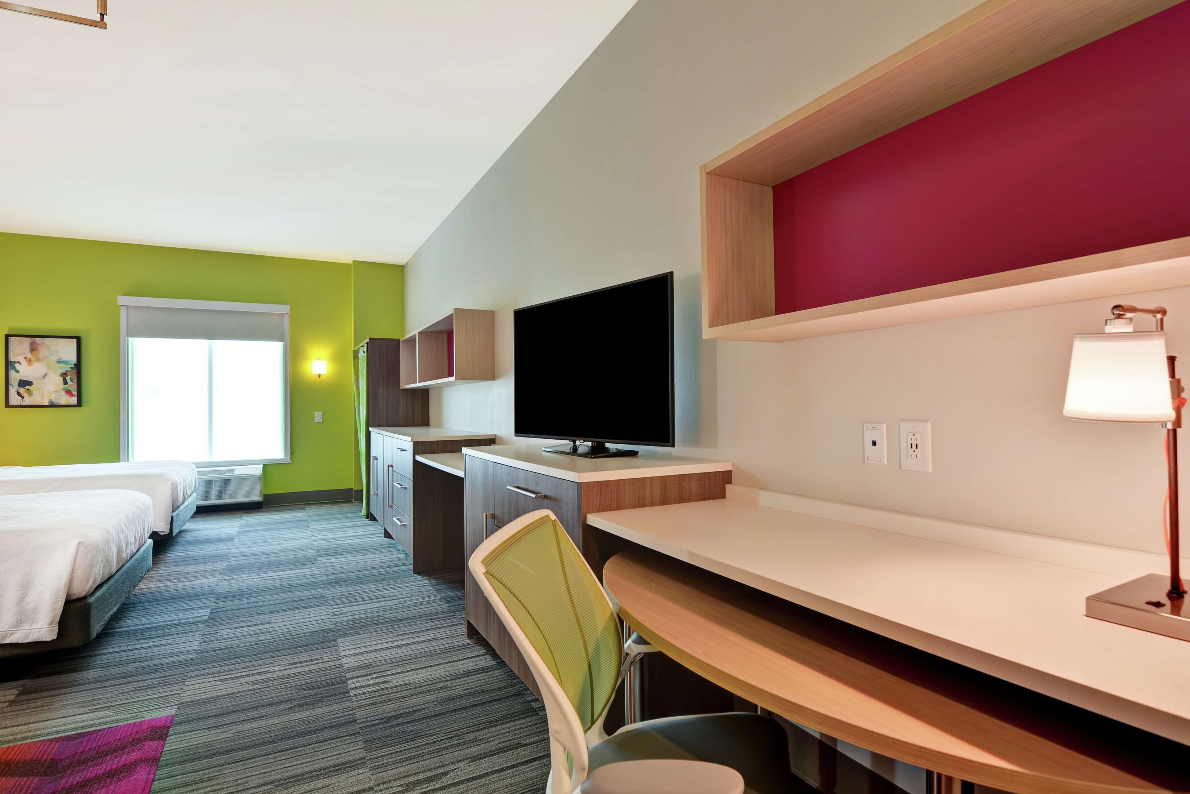 Habitación de hotel con dos camas, un escritorio con una computadora, un televisor y una ventana.