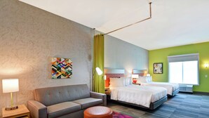 Ein Hotelzimmer mit einer Couch, zwei Betten, einem bunten Teppich und einem Bild an der Wand.