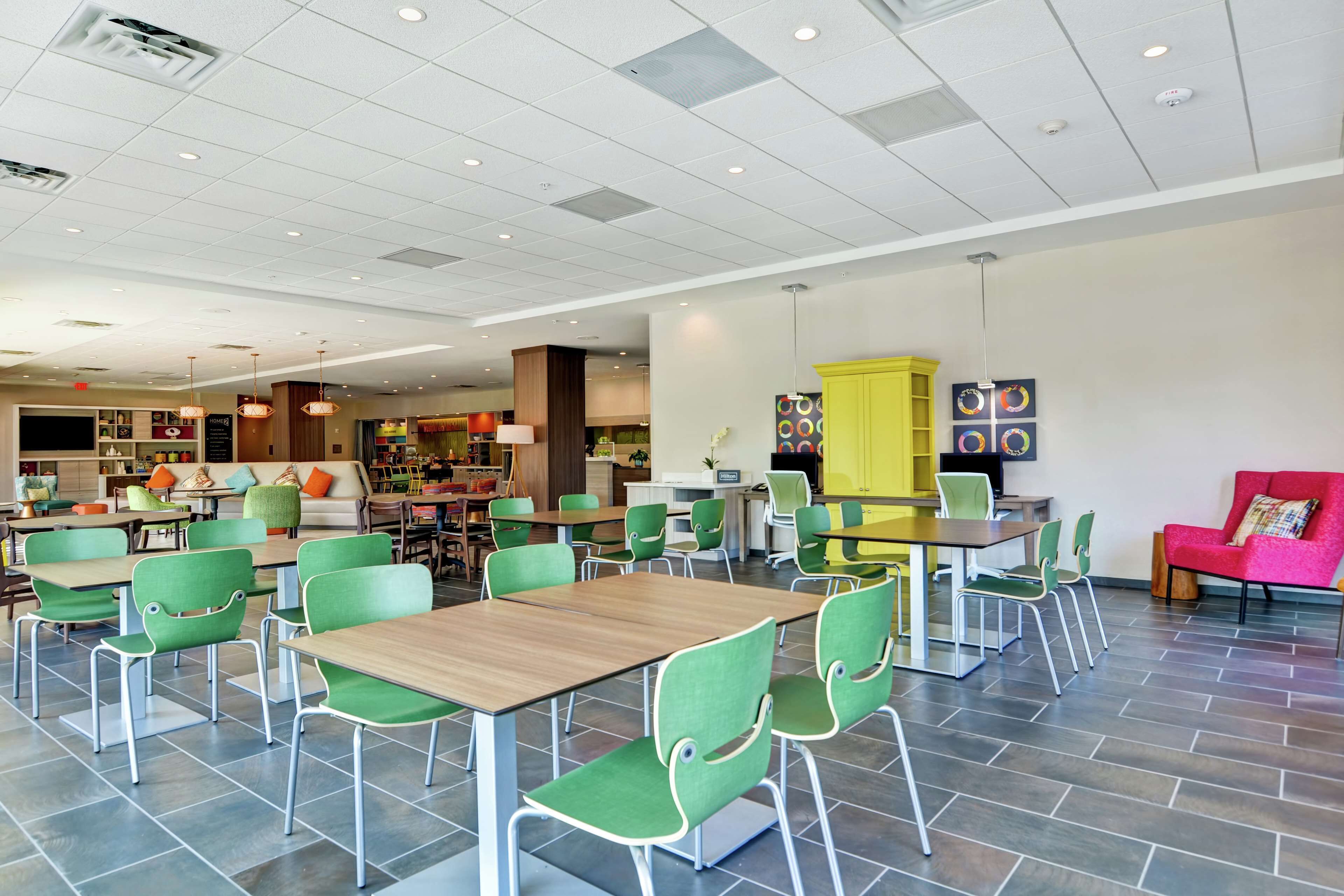 A modern dining area with green chairs and wooden tables, a yellow cabinet, and a red sofa.