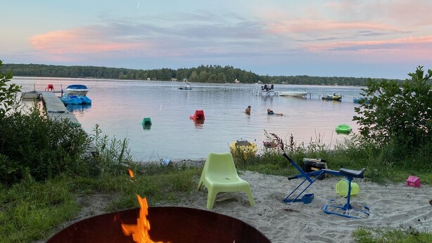 En vacker plats vid sjön med en eldstad, utomhusstolar och båtar på vattnet.