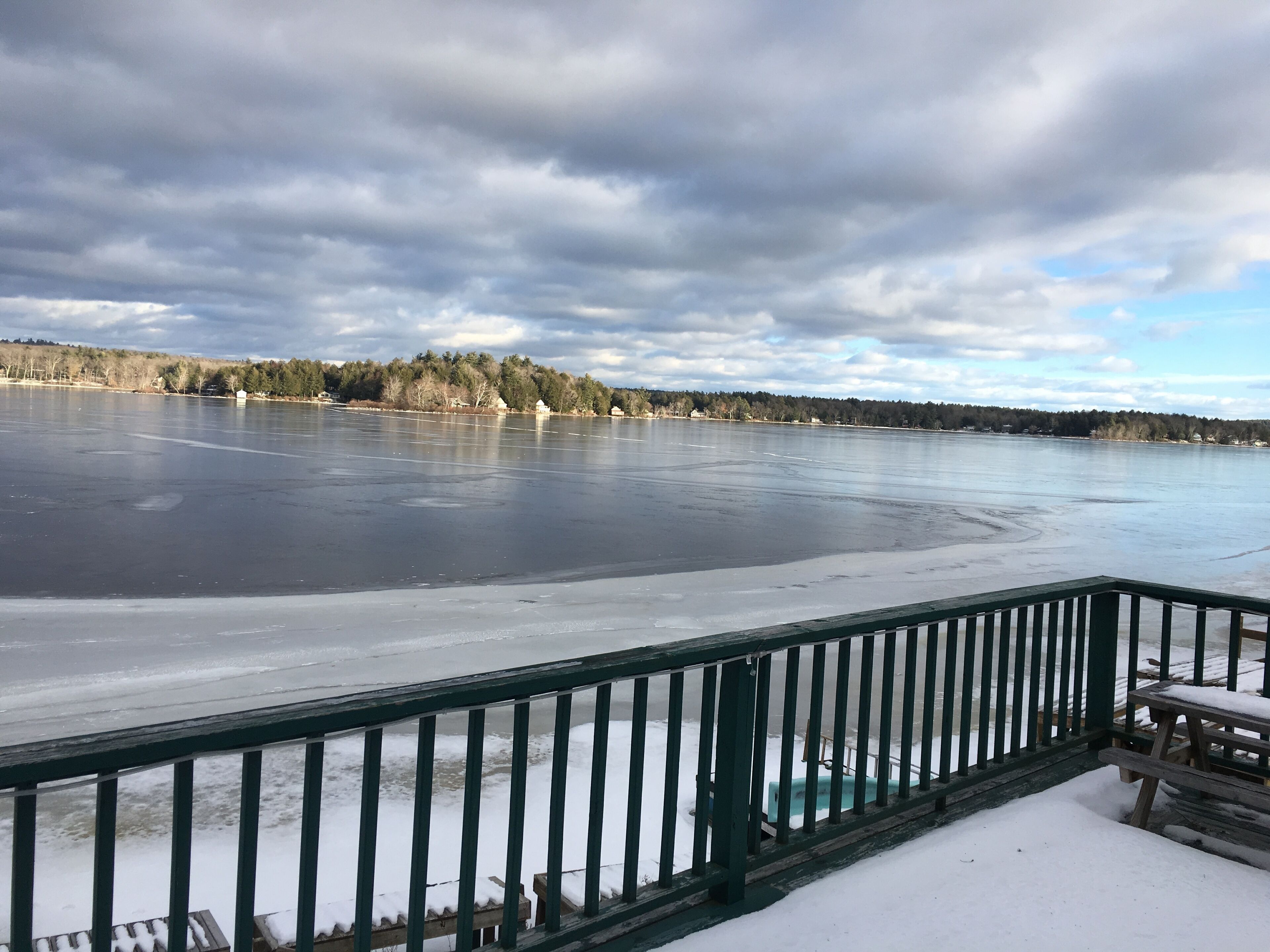 A frozen lake with a wooden deck and railing in the foreground.