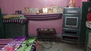 A small, dimly lit room with pink walls, a bunk bed, a small table with religious items, and a television. - Dandak Tribes Homestay and Tourism group! Bastar Homestay! (dantewada)