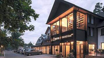 A hotel with a prominent sign, large windows, and a parking area with cars.