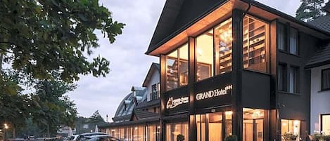A hotel with a prominent sign, large windows, and a parking area with cars.