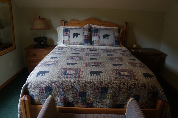 A bed with a quilt featuring animal patterns, a wooden headboard, a nightstand with a lamp, and a mirror on the wall.