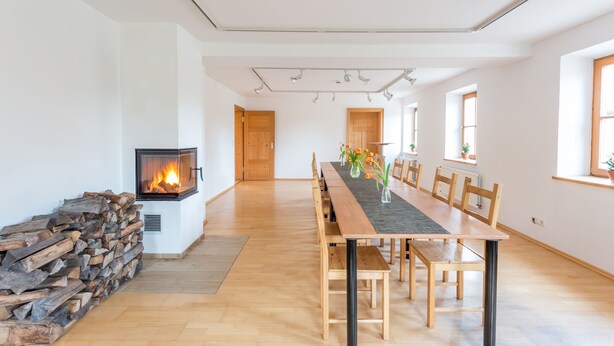 Ein geräumiger Essbereich mit einem langen Holztisch, Stühlen, einem Kamin und Blick auf den angrenzenden Raum.