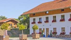 Ein Gebäude mit roten Ziegeln, weißen Wänden und zahlreichen Fenstern mit Blumenkästen. Im Vordergrund befinden sich Bäume und Holz-Pflanzgefäße.