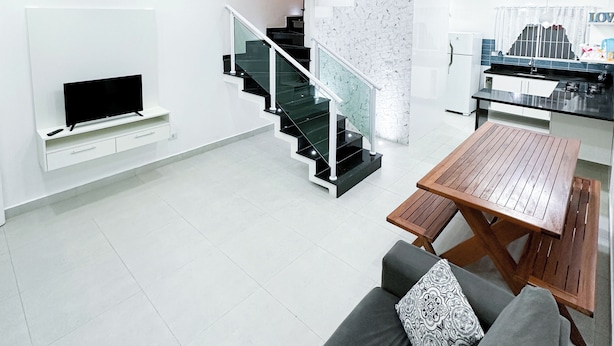 Ein modernes Wohnzimmer mit Flachbildfernseher, einem Holzesstisch, einem grauen Sofa und einer Wendeltreppe.