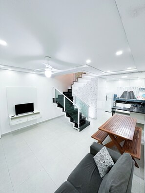 A modern living room with a flat-screen TV, a wooden dining table, a gray sofa, and a spiral staircase. - House for vacation in Maranduba/ Ubatuba  (Maranduba)