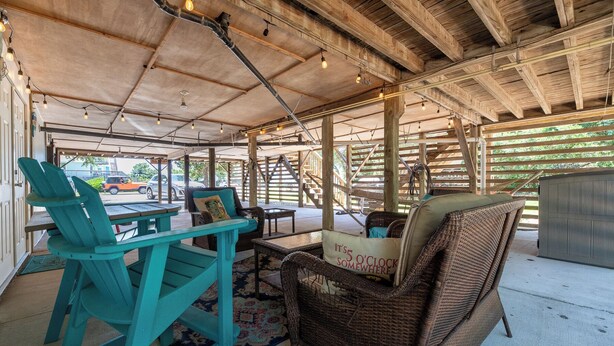 A covered outdoor seating area with wooden beams, wicker furniture, and a table with chairs. - Landing Pad - Kill Devil Hills, Oceanside, 350 Yards to Beach, YR Flex Stays, 4 BR (Kill Devil Hills)