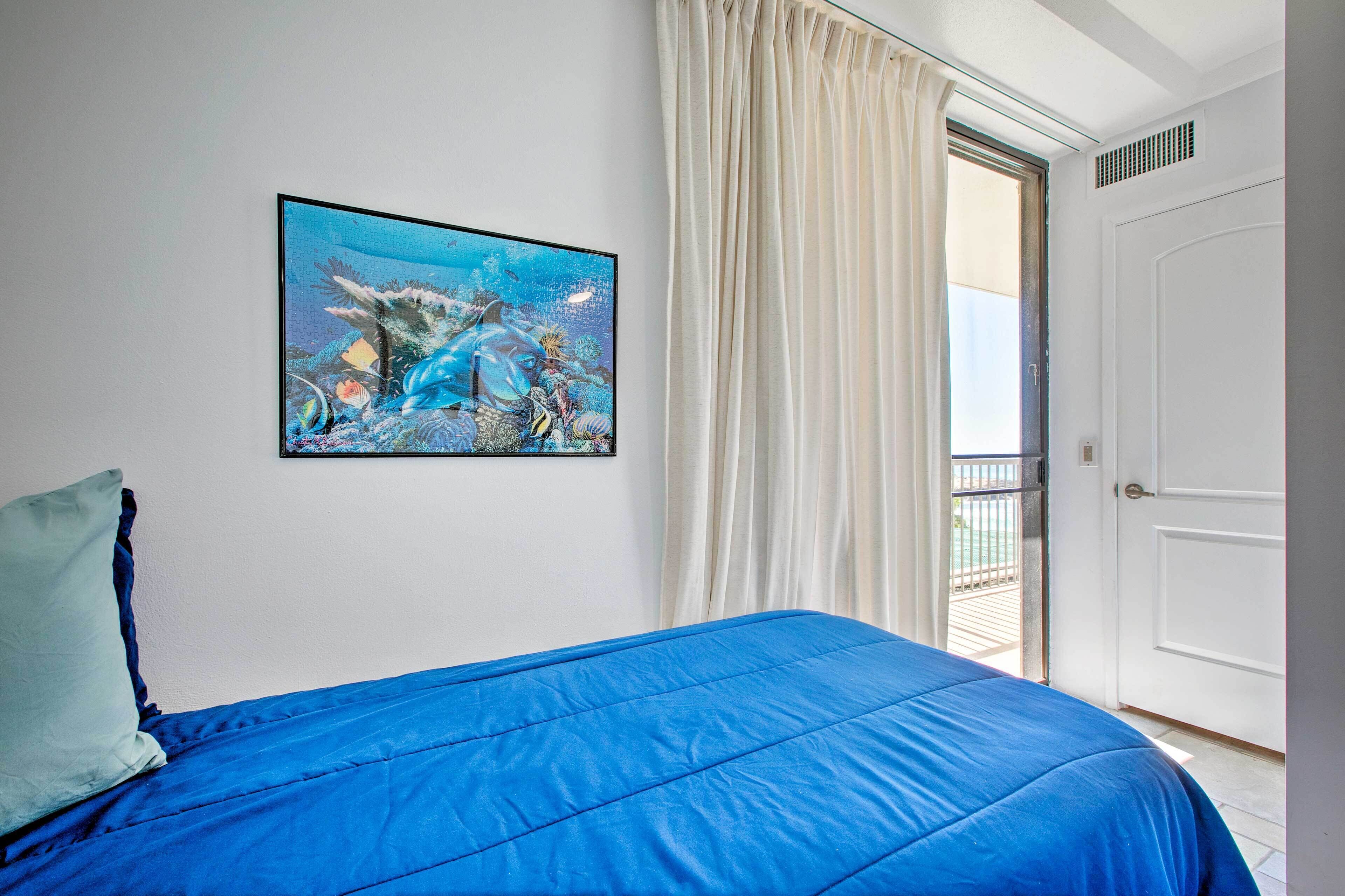 Een slaapkamer met een blauw bed, een schilderij van een onderwaterlandschap en een deur die uitkomt op een balkon.
