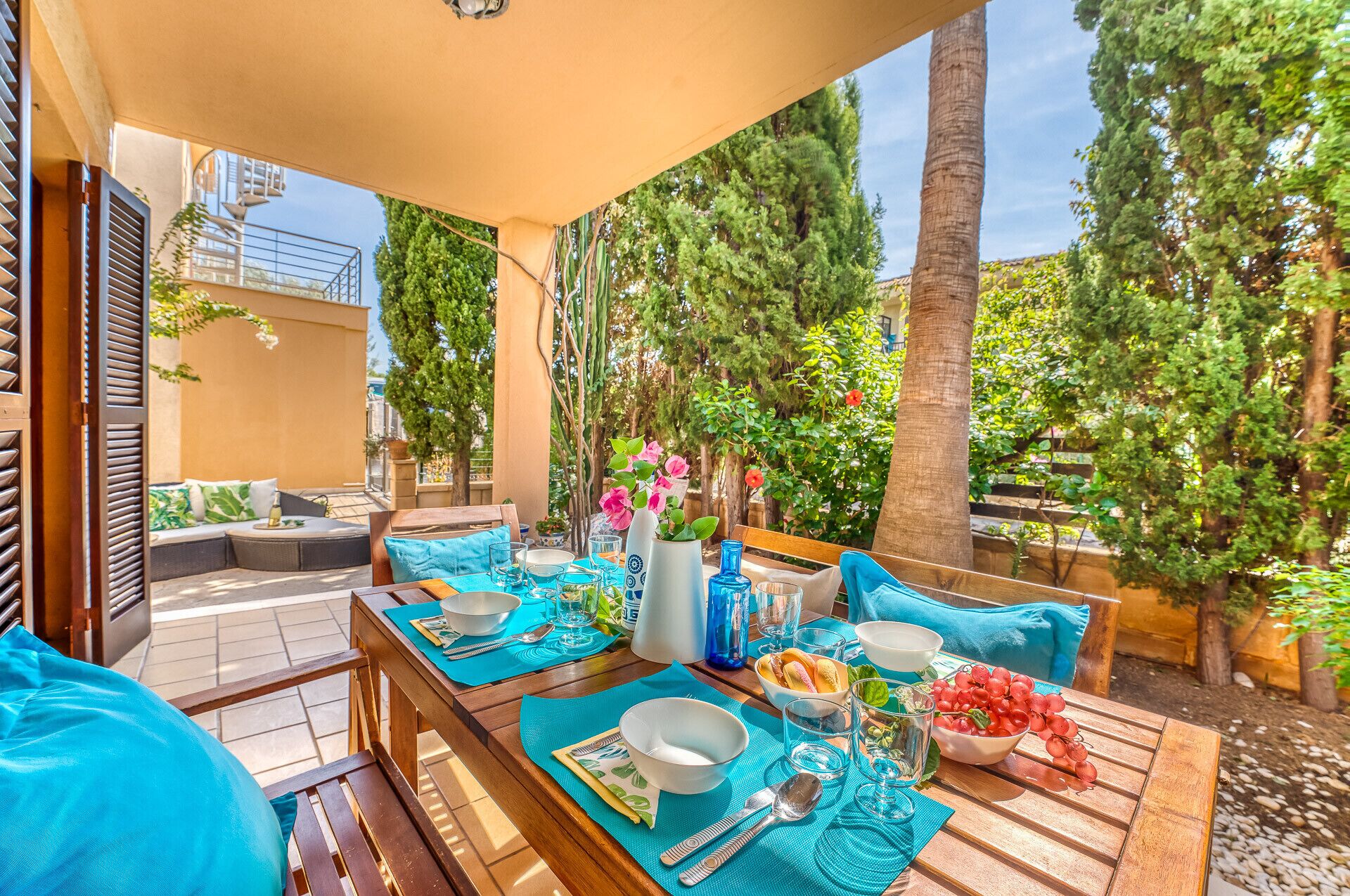 An outdoor dining area with wooden tables, blue cushions, and a variety of dishes and drinks.