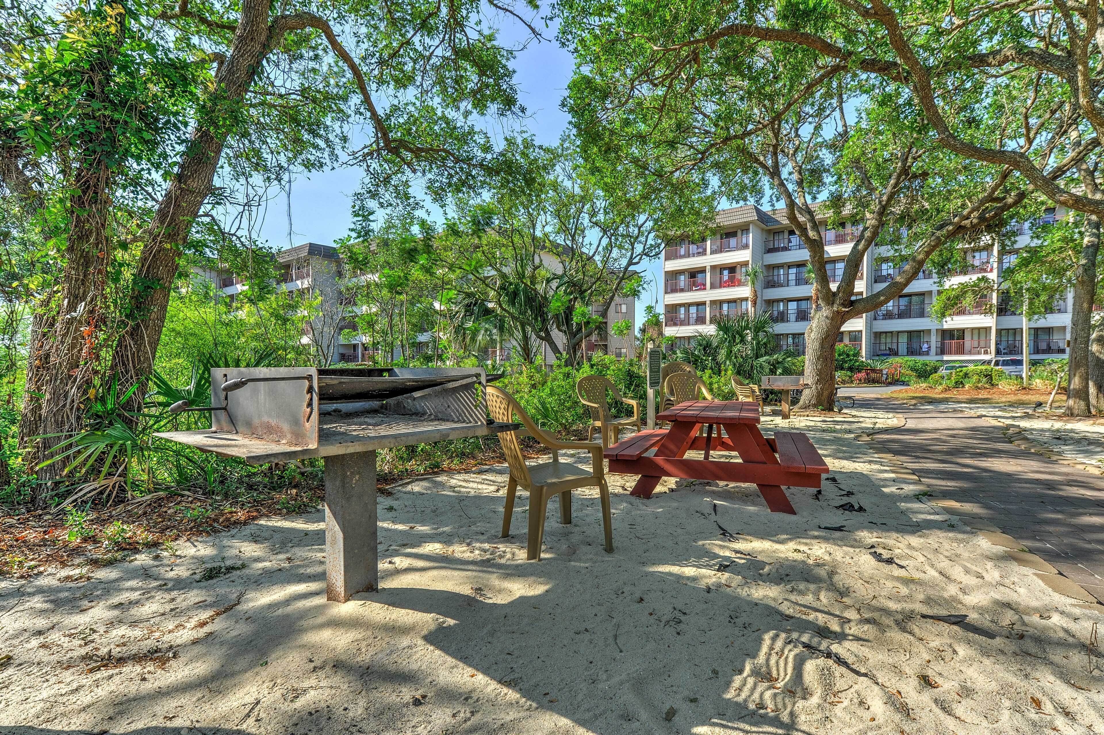 A sandy outdoor area with a barbecue grill, picnic table, and chairs.