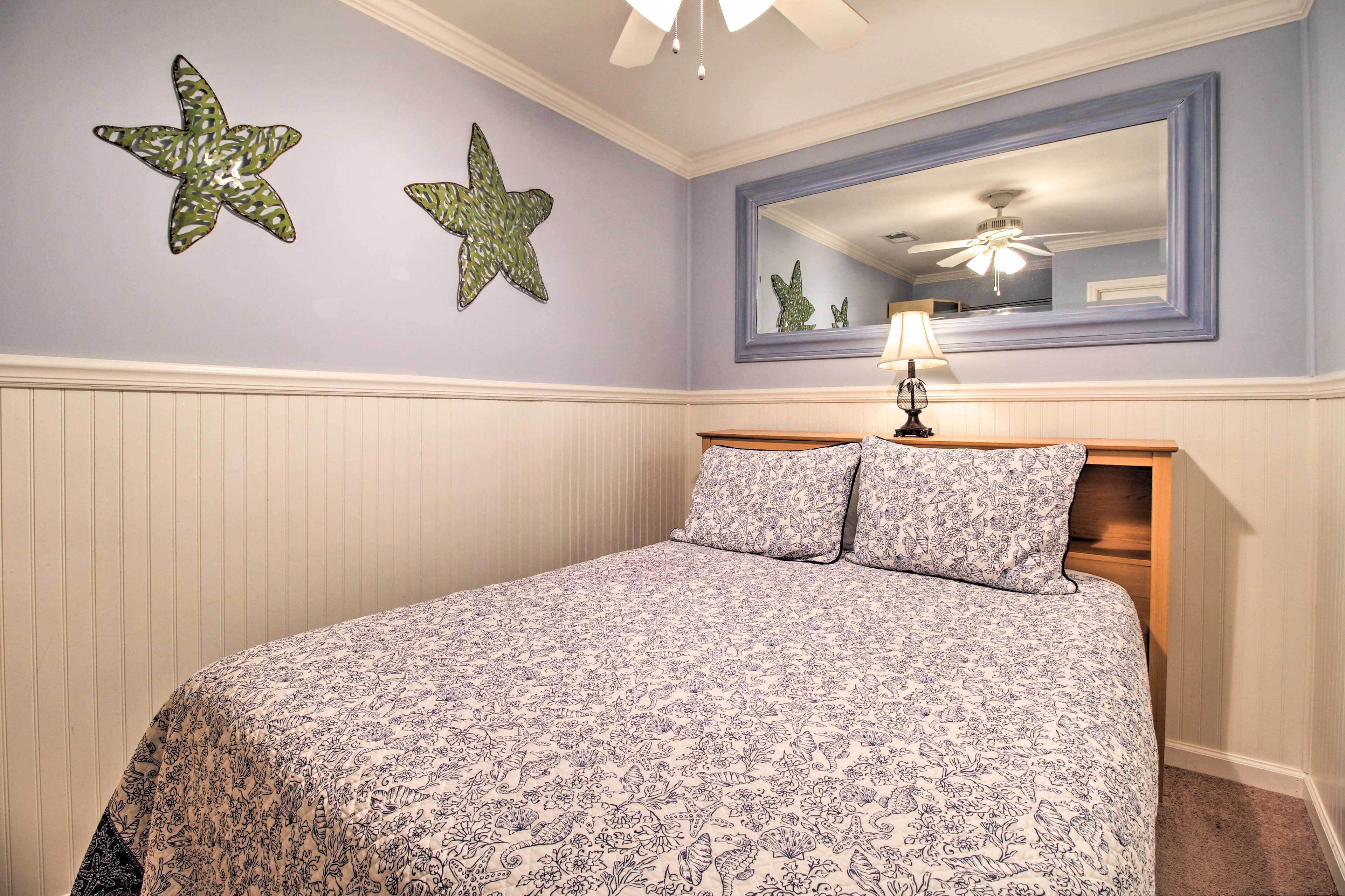 A bedroom with a bed, two starfish wall decorations, a ceiling fan, and a large mirror above the bed.