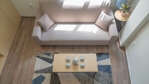 Ein modernes Wohnzimmer mit einem beigen Sofa, einem Couchtisch aus Holz mit Teekannen und einem gemusterten Teppich.
