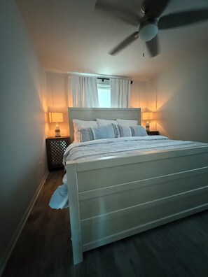 Une chambre à coucher avec un lit, un ventilateur de plafond, des lampes de chevet et une fenêtre avec des rideaux.