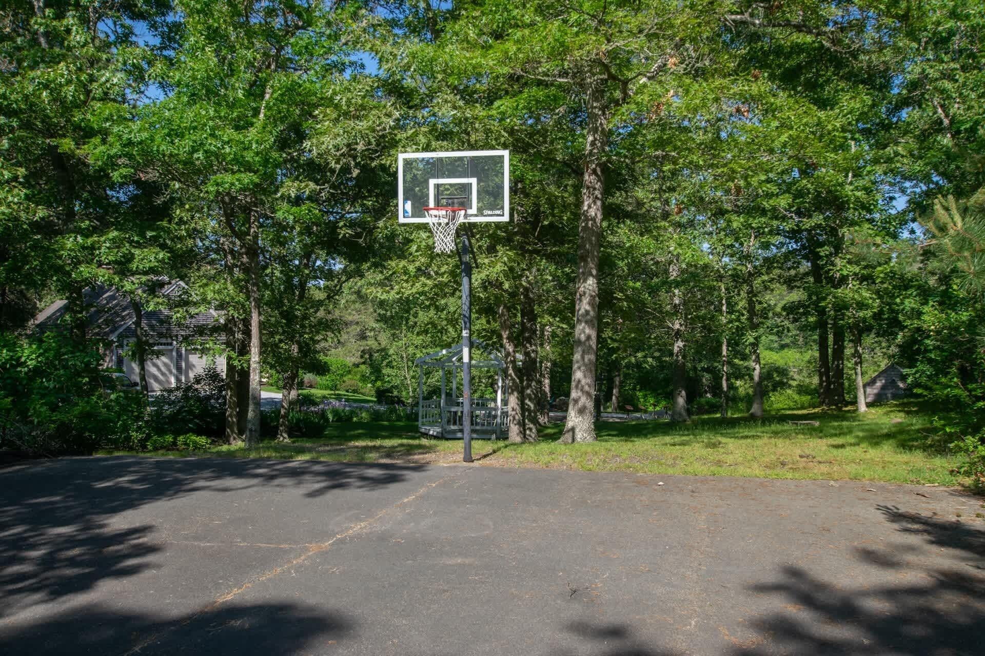 An outdoor basketball court surrounded by trees and a house in the background.