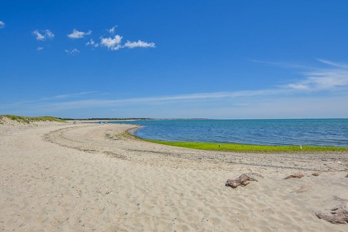 Ein sandiger Strand mit blauem Himmel und ruhigem Meer.