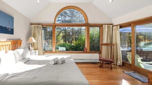 A spacious bedroom with a large bed, a wooden floor, a large arched window, and a view of the outdoors.
