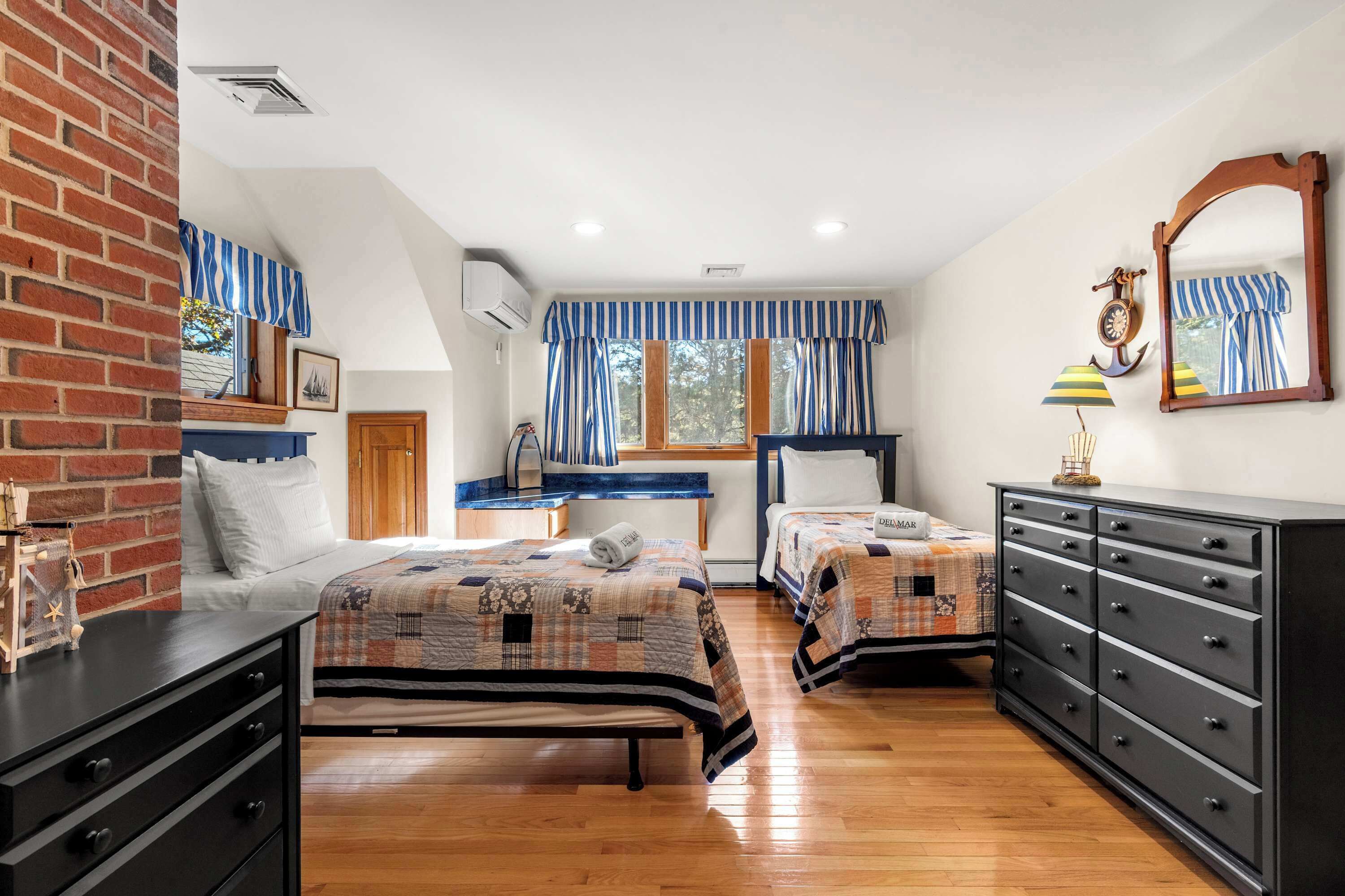 A bedroom with two beds, a dresser, a vanity, and a window with striped curtains.