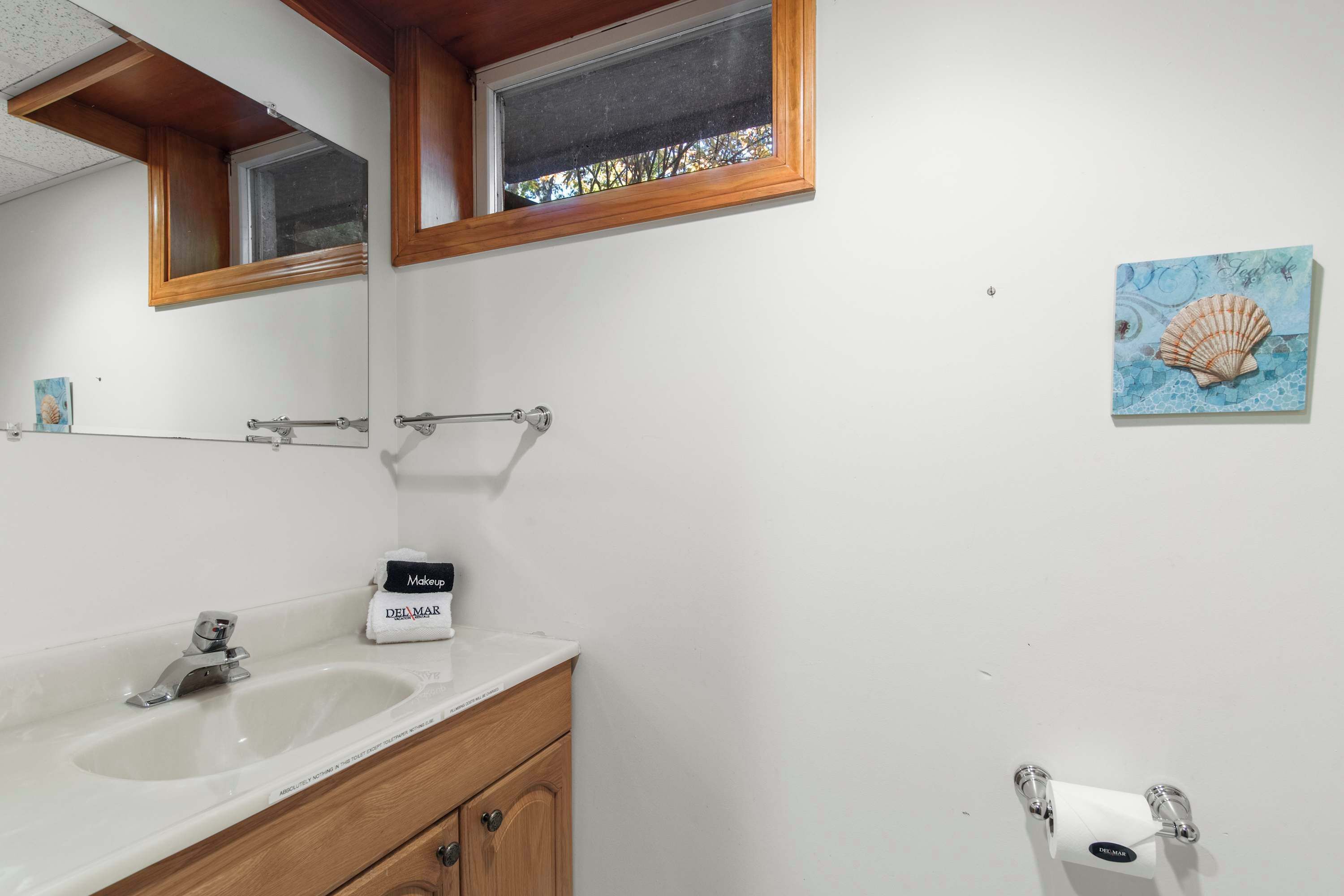 A bathroom with a white sink, wooden vanity, a mirror, a towel rack, and a painting of a seashell.