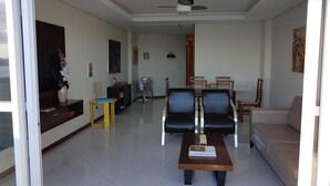 A living room with a sofa, a coffee table, a dining table with chairs, a TV, and a ceiling fan. - INCREADIBLE VIEW! UNFORGETABLE PLACE! YOU MUST TRY IT! (Guarapari)