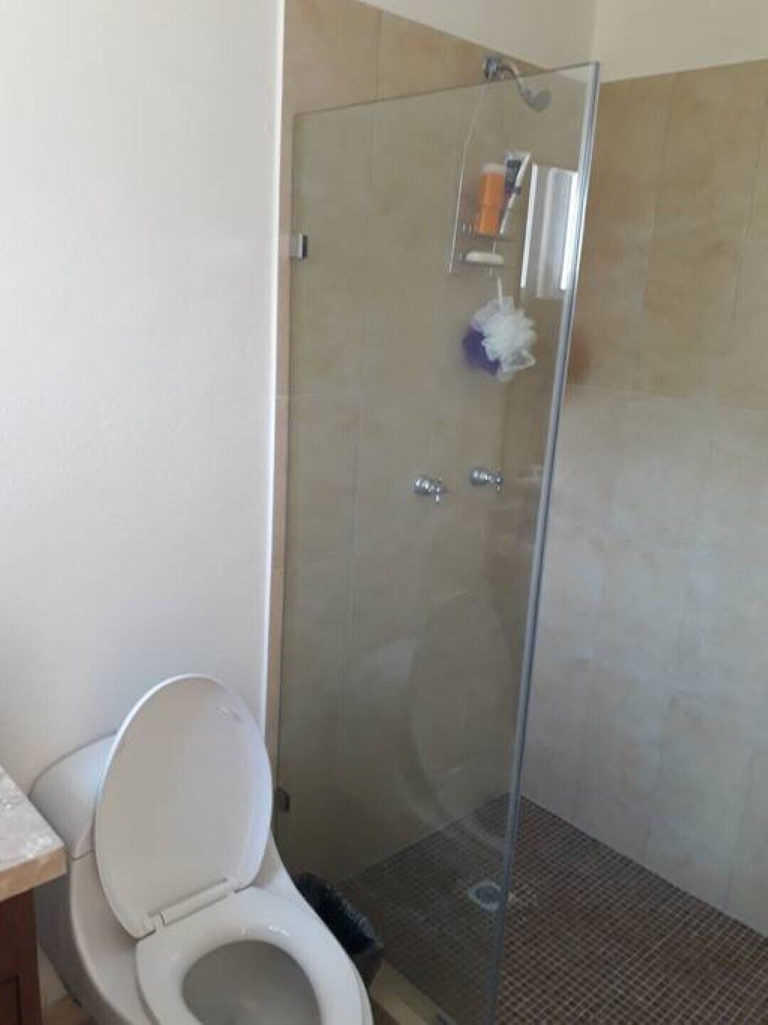 A bathroom with a toilet, a glass shower enclosure, and tiled walls.