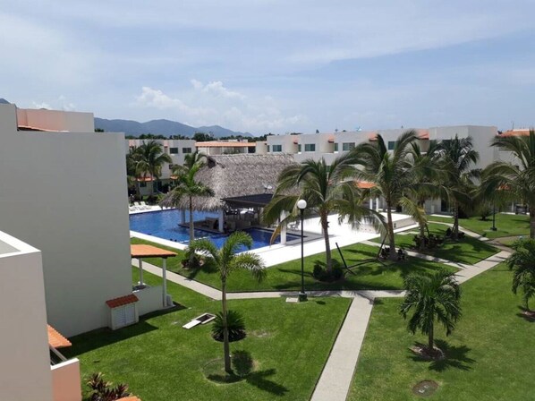 Un resort con piscina rodeada de palmeras y una estructura de techo de paja.