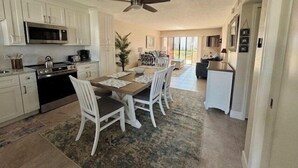 A spacious kitchen with white cabinetry, a microwave, and a stove. There is a dining area with a wooden table and white chairs. A ceiling fan is visible above the dining area. - Runaway Bay 135 - Beach, Pool, gym and bay (Bradenton Beach)