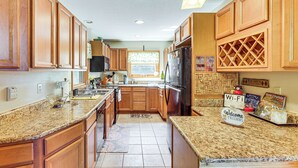 A kitchen with wooden cabinets, granite countertops, a refrigerator, and a window with a view.