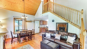 A spacious living room with a wooden ceiling, a leather sofa, a dining table with chairs, and a staircase leading to an upper level.