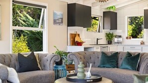 Una sala de estar moderna con un sofá gris, una mesa redonda de centro y una cocina al fondo.