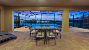 A covered outdoor dining area with a view of a swimming pool and surrounding landscape. - Kids Bedrooms | Games | Screened Pool | Near Attractions (Kissimmee)