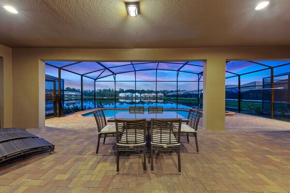 A covered outdoor dining area with a view of a swimming pool and surrounding landscape. - Kids Bedrooms | Games | Screened Pool | Near Attractions (Kissimmee)
