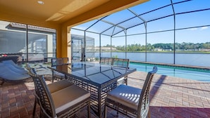 A covered outdoor patio with a glass table and chairs, overlooking a lake. - Kids Bedrooms | Games | Screened Pool | Near Attractions (Kissimmee)