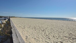 Una playa arenosa con un camino de madera y coches aparcados.