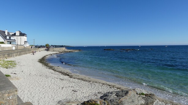A coastal beach with a sandy shore, a stone wall, and a few buildings in the background. - L'Ilôt Bateau apartment very close to the corniche for 2 people (Concarneau)