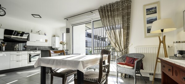 Une cuisine moderne avec un coin repas, une chaise en osier et une table mise pour deux personnes.